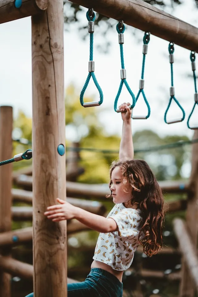 A child swinging from the rings of an outdoor climbing frame