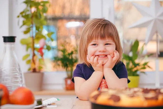 A smiling child at the table, chin resting on both hands