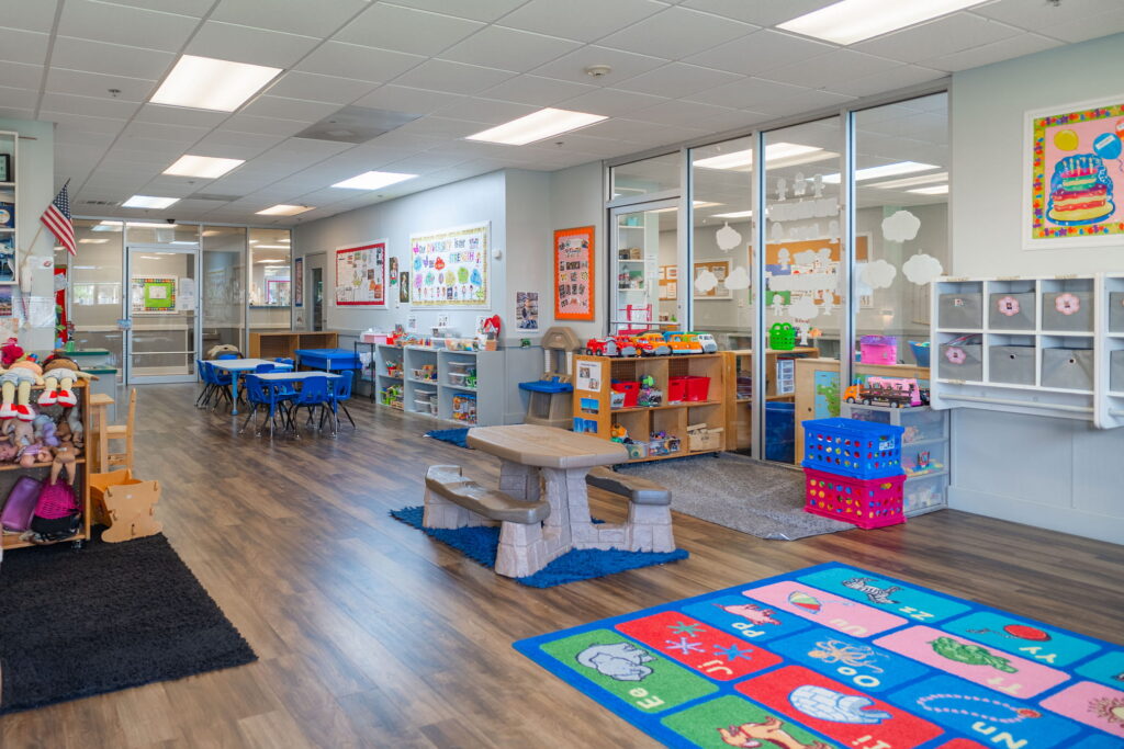 A classroom play area with a picnic table, a play kitchen and a letter rug