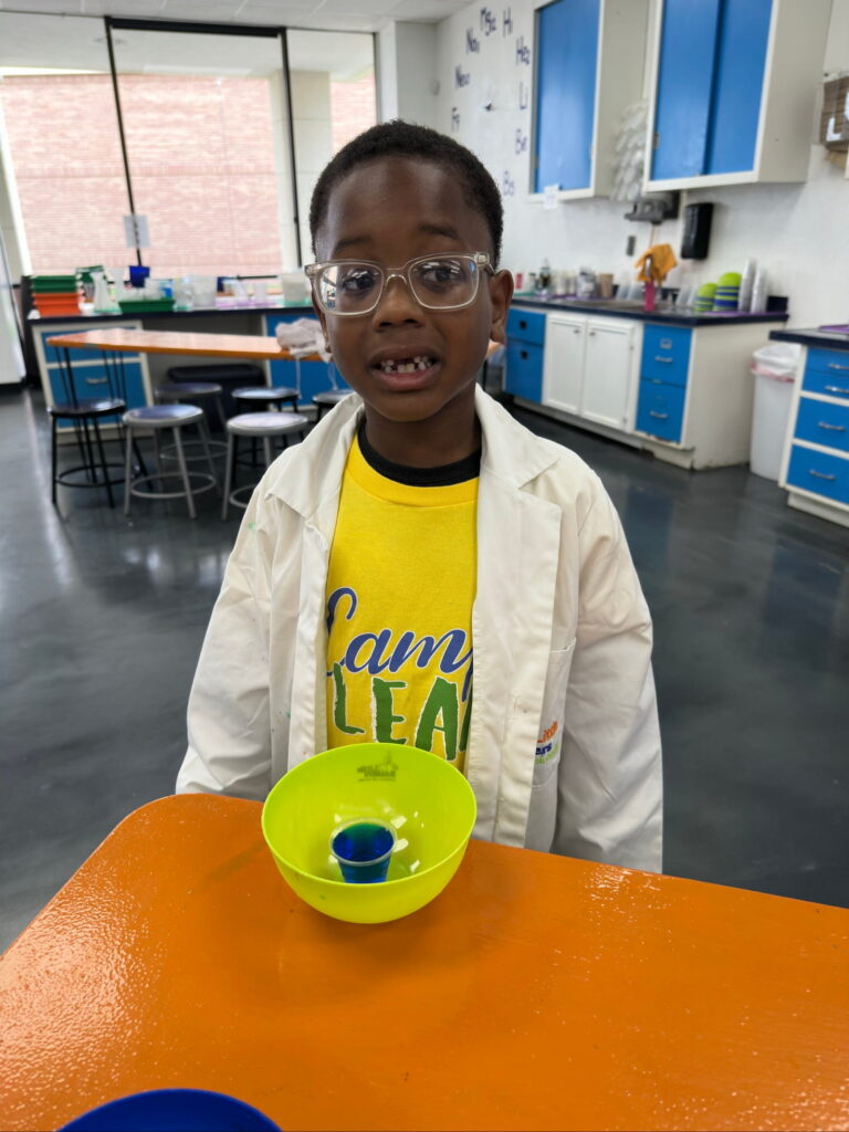 A child in a lab coat watching a colour-mixing science experiment