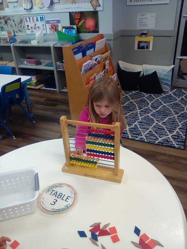 A child using a wooden abacus at a classroom table